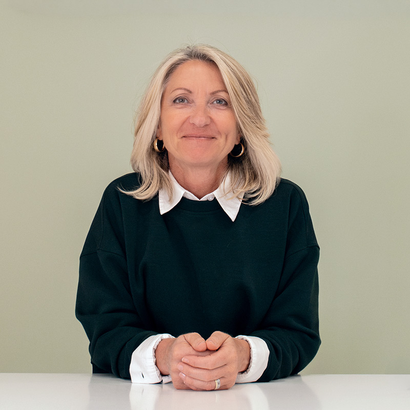 LEBENSKOMPONISTIN® Barbara Schwab-Melcher sitzt an ihrem Arbeitsplatz mit lächelndem klarem Blick direkt in die Kamera