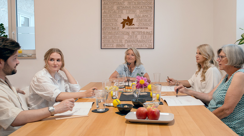 LEBENSKOMPONISTIN® Barbara Schwab-Melcher in einem Workshop-Coaching am Kopfende eines gossen Arbeitstisches, flnkiert von jeweils zwei Personen auf der rechten, als auch linken Tischseite